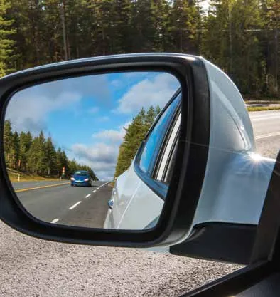 Car door mirror showing the road behind with a following vehicle