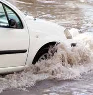 White car driving through deep flood water, throwing up spray