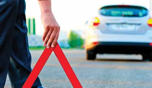 Person placing a red warning triangle on the road behind a stopped car