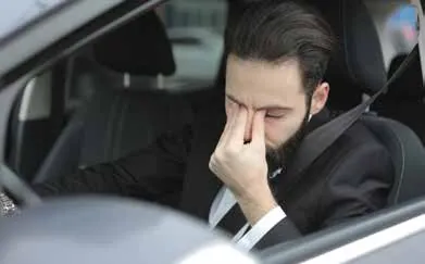 Tired man in a car rubbing his eyes